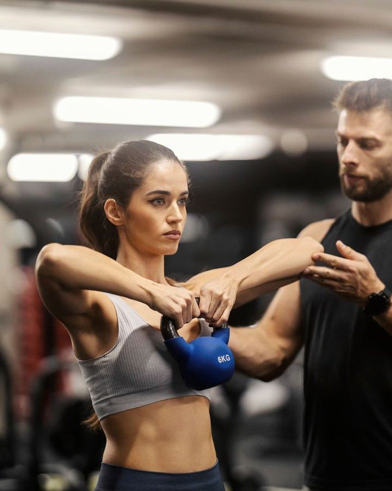 Coach guiding a member through a kettlebell exercise
